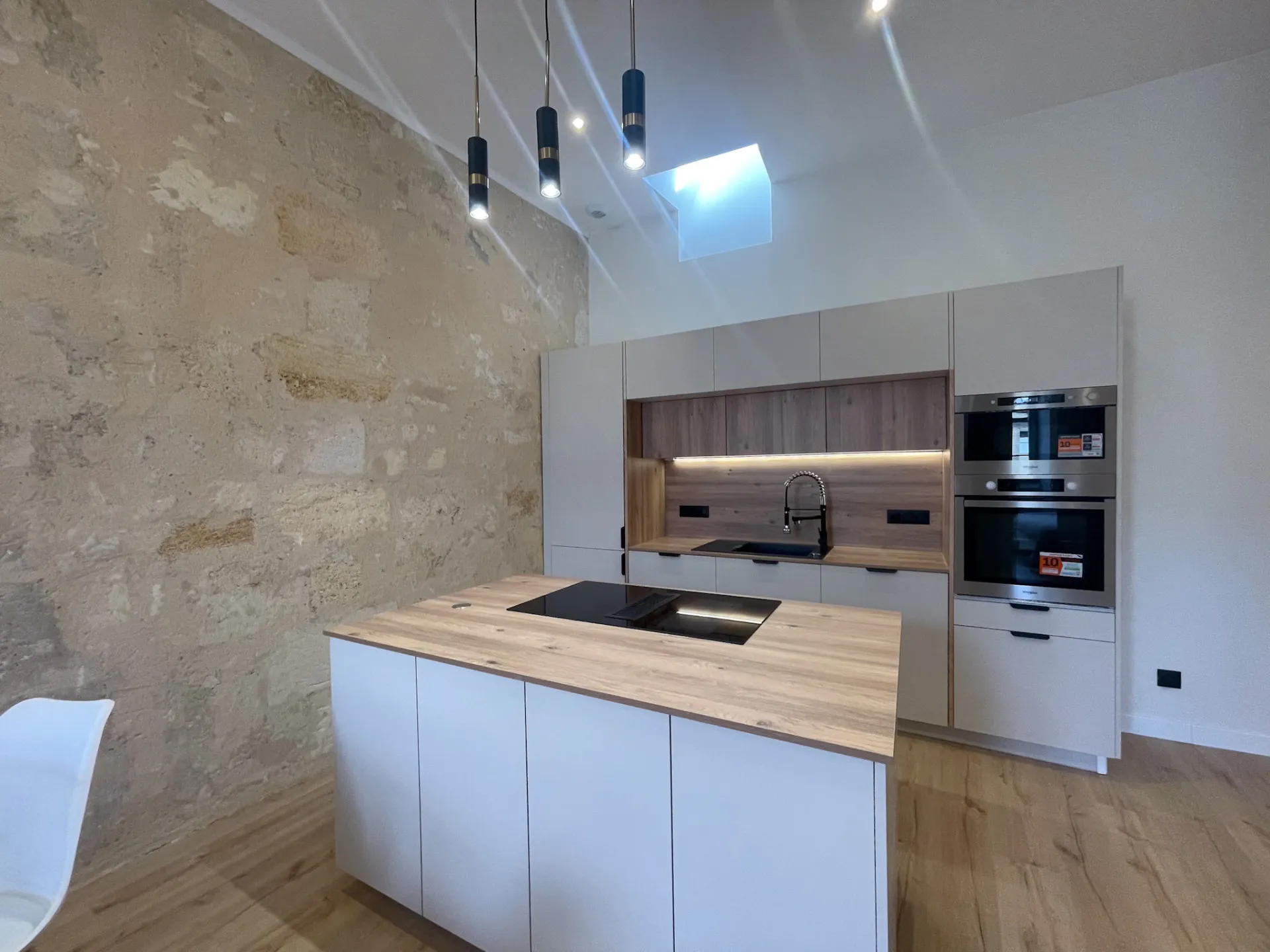 Cuisine équipée rénovée contre un mur en pierre apparente, îlot central et bois clair