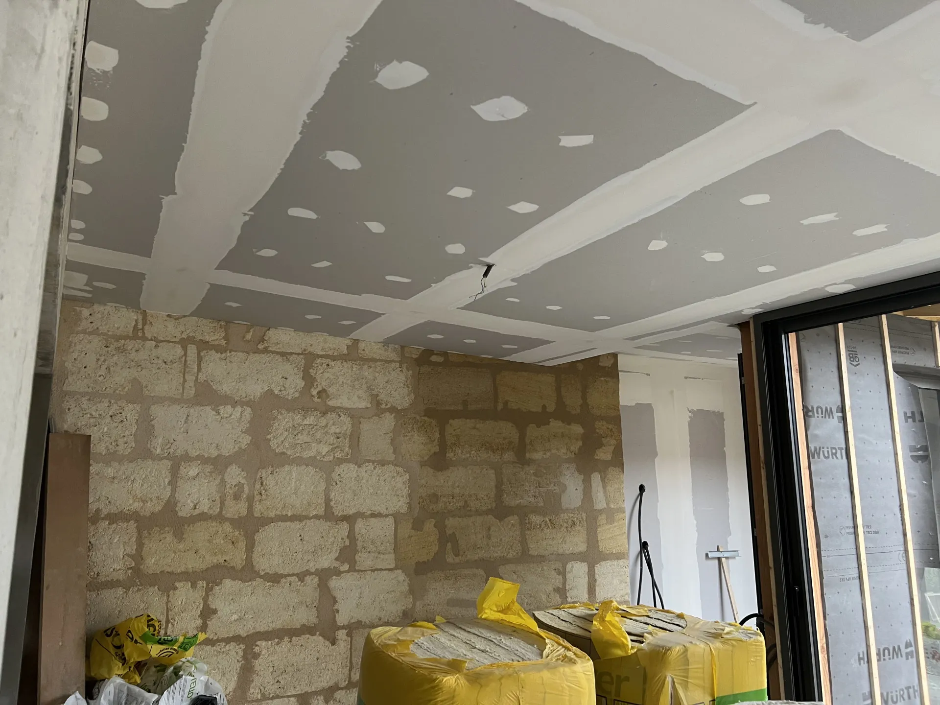Plafond en plaques de plâtre jointoyé et isolation en laine de roche contre un mur en pierre