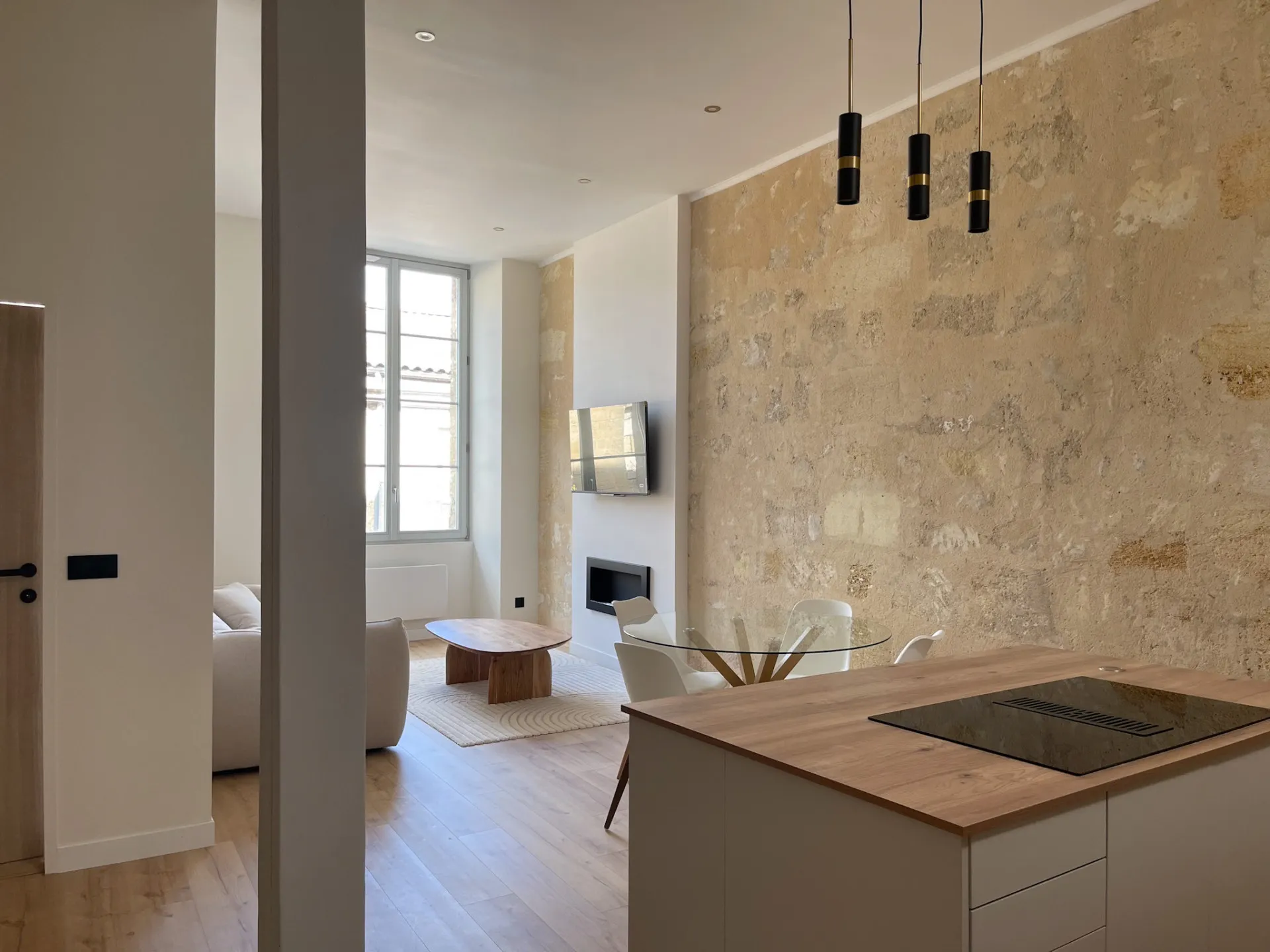 Appartement rénové à Bordeaux : mur en pierre apparente, cuisine ouverte et suspensions noires